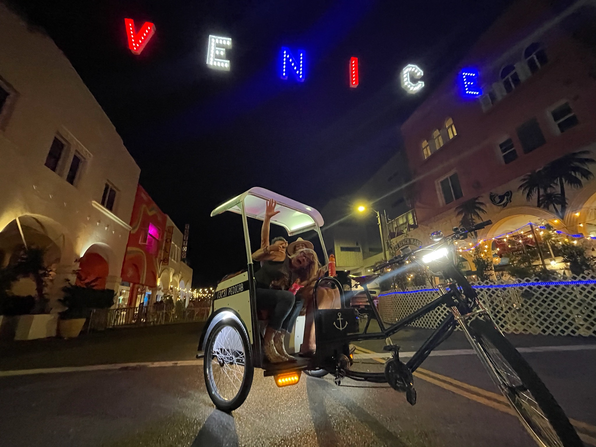 A Beach Buggy pedicab passing under the lit Venice sign on Independence Day.